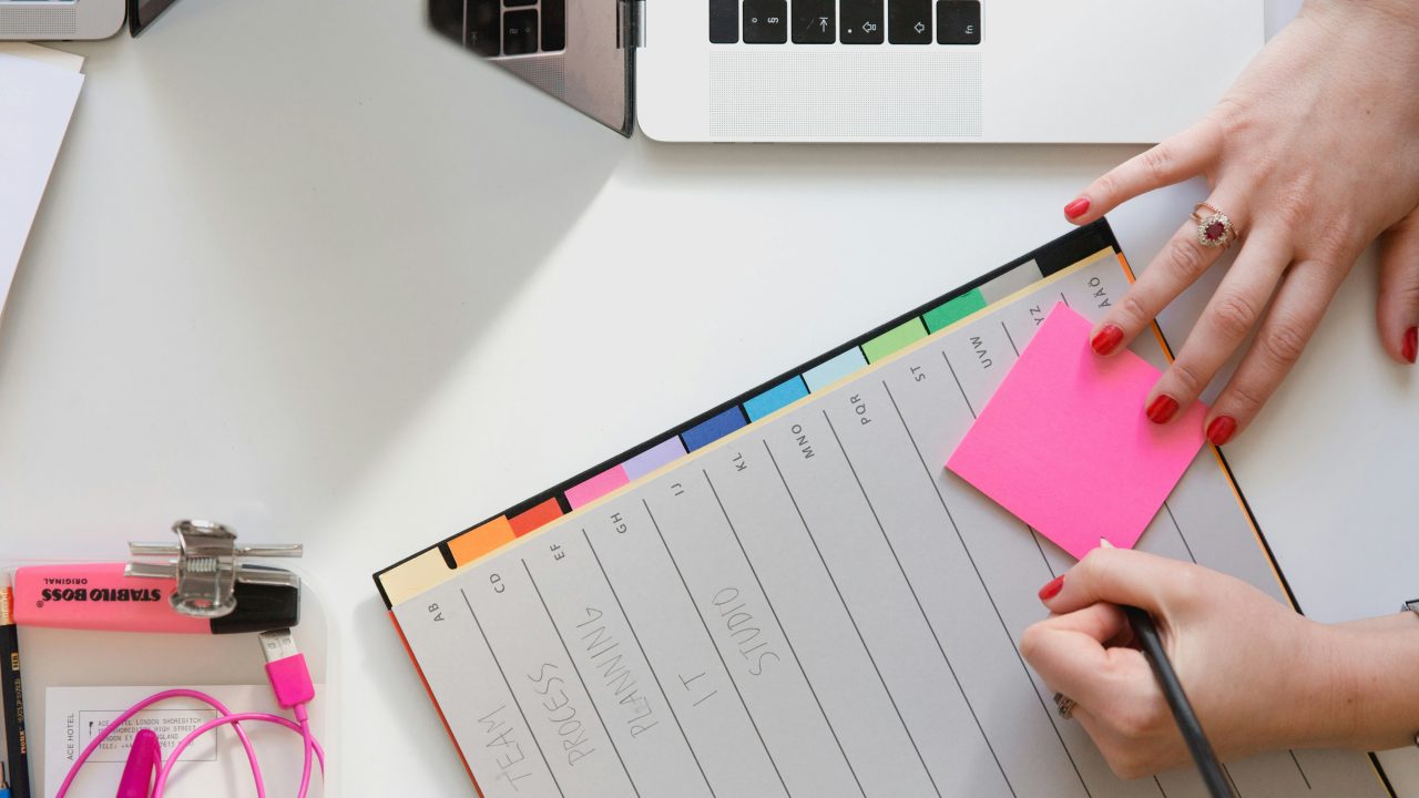 feminine hands writing on a sticky note on top of a planner