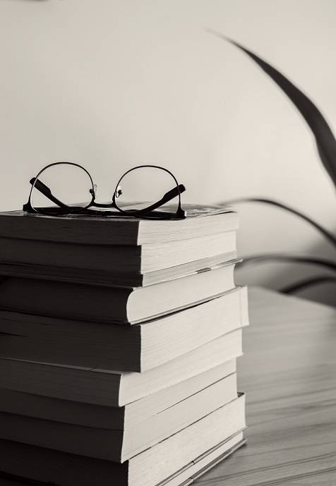 a stack of books near a plant and a pair of glasses on top