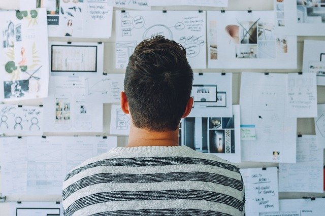 the back of a man's head looking at a whiteboard with various notes and layouts about business and infrastructure