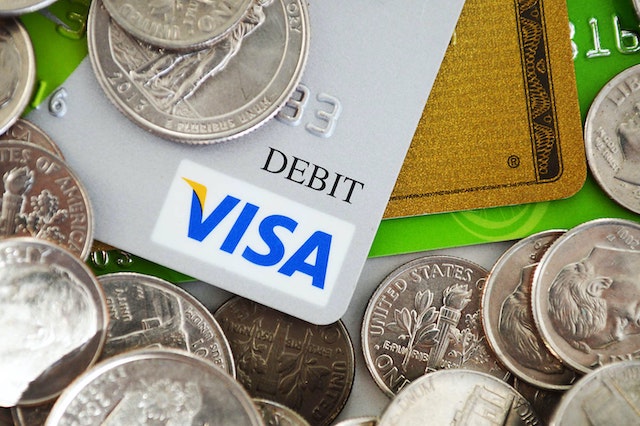 close up of a debit card with various coins from all around the world on top