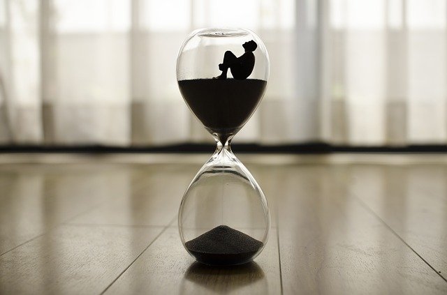 a silhouette of a man in the top of an hourglass as sand trickles into the bottom half of the hourglass