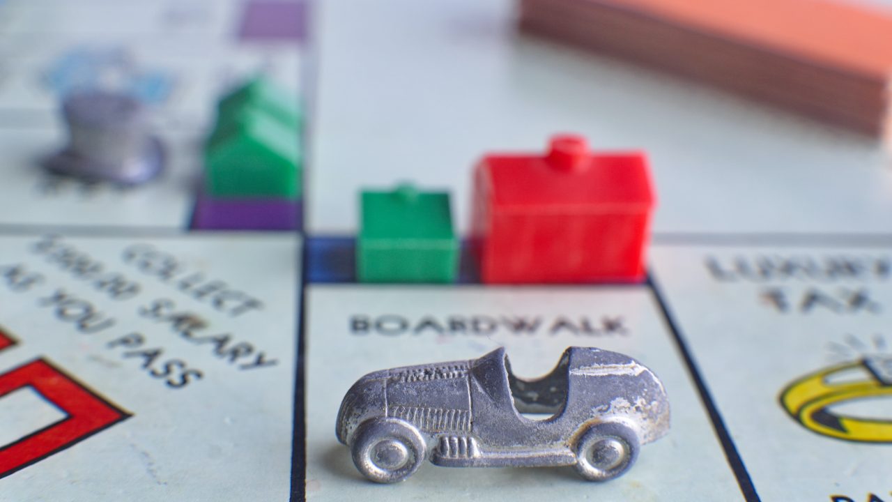 close up of a monopoly board game with the car piece on boardwalk with a house and hotel on it