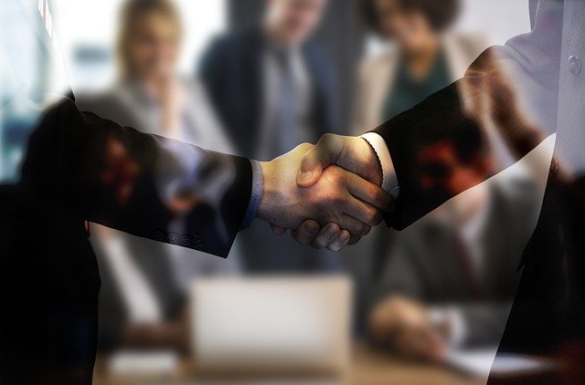 a handshake superimposed in front of several employees at a conference table