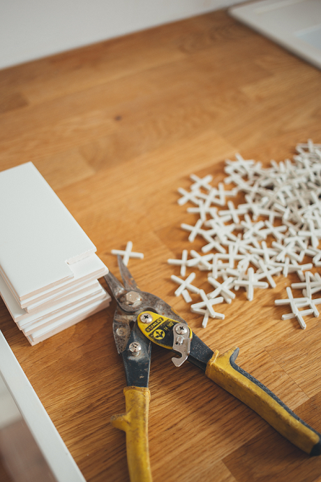Pliers, tiles, and spacers laid out on a kitchen counter in front of a half-completed backsplash.